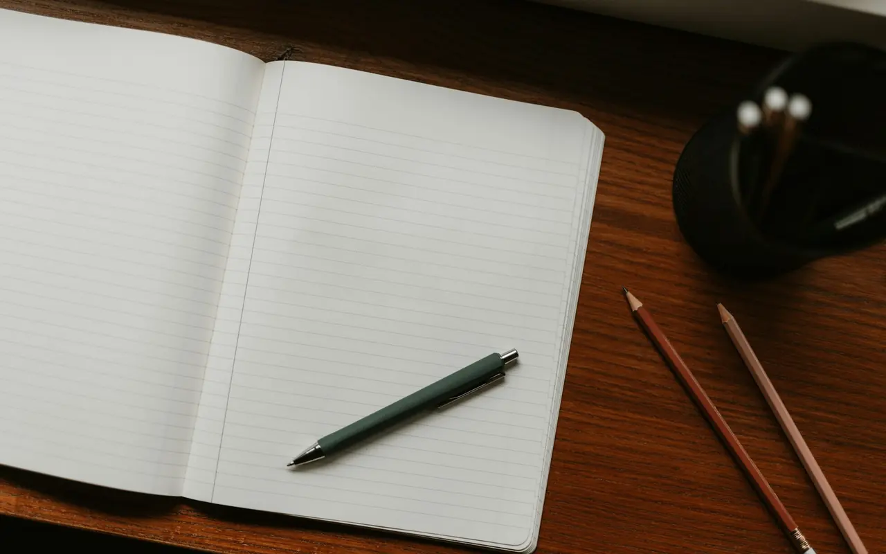 Open notebook with pens and pencils on a wooden desk