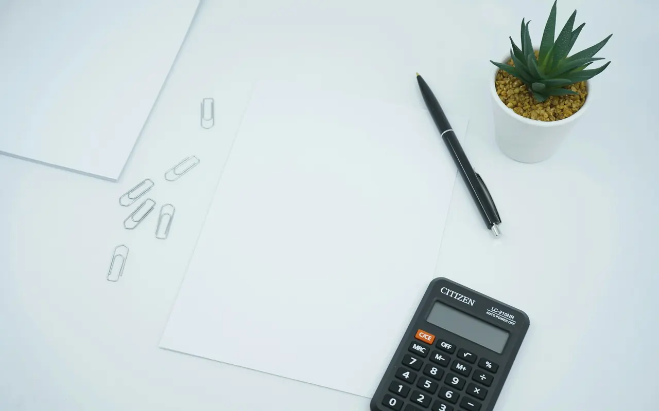 Calculator and pen beside a blank sheet of paper