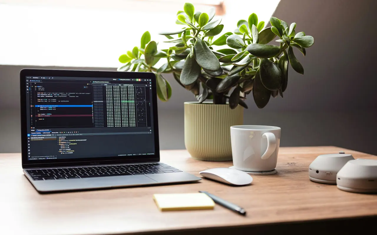 Laptop showing code beside a plant and a mug