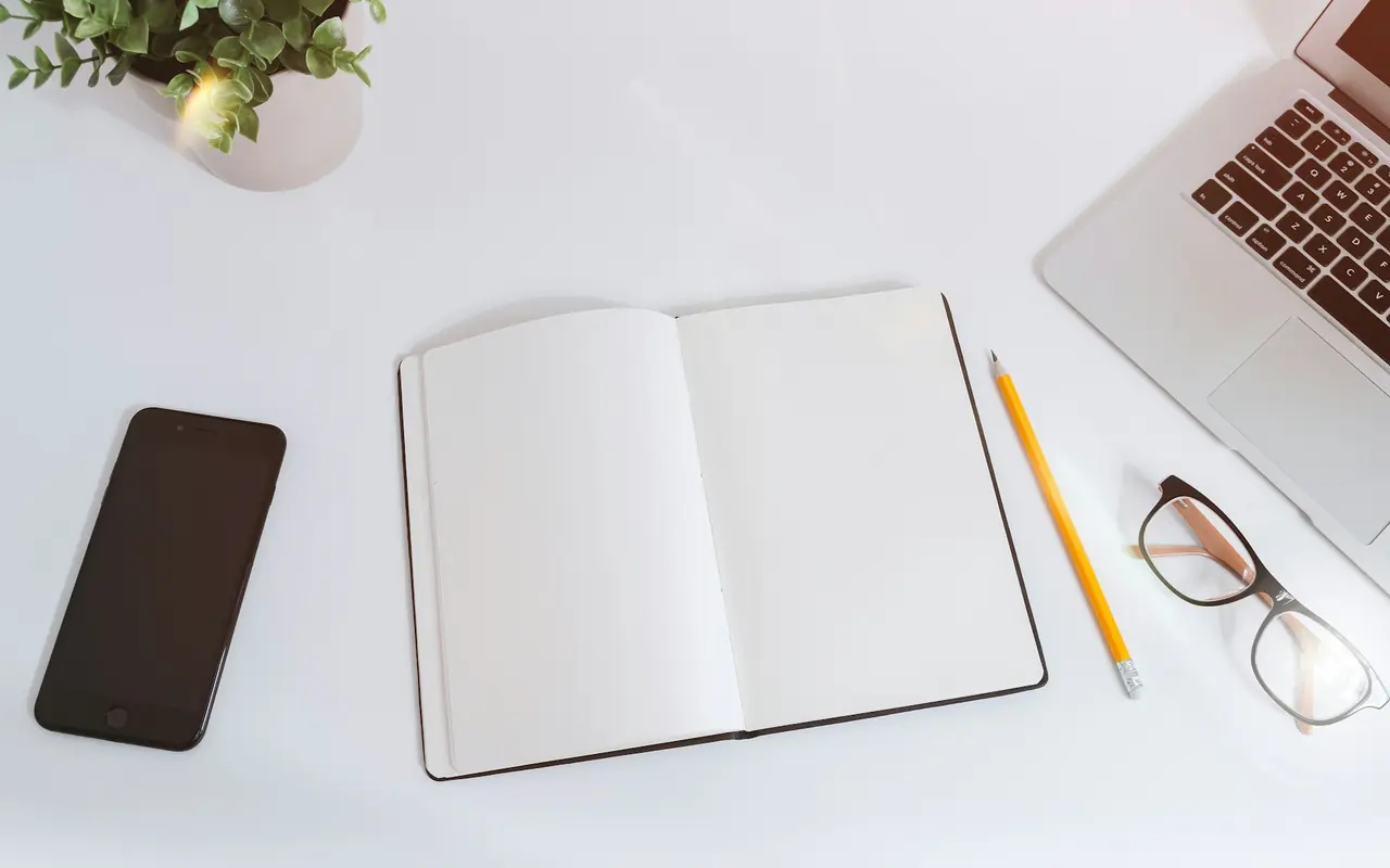 Open notebook with a laptop and phone on a white desk