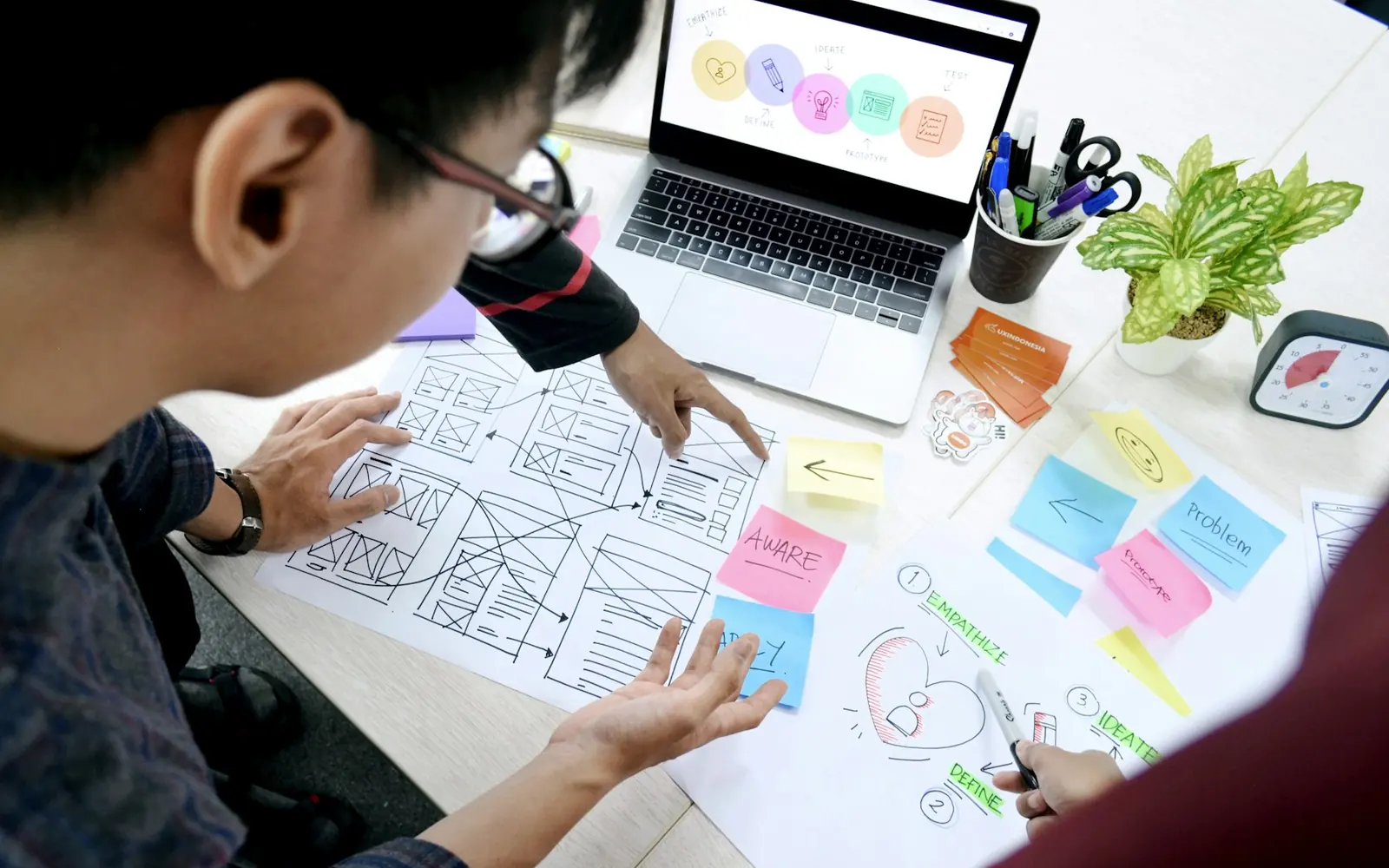 Designer sketching website wireframes beside a laptop